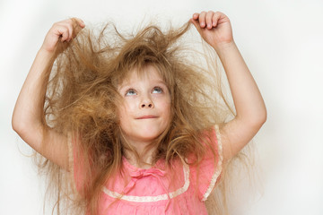 a little girl with tangled long hair in a pink dress on a white background tries to comb it. naughty hair portrait woman with a comb doesn't know what to do