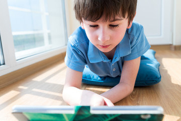 Naklejka premium Nine years old child using tablet lying on pillow. Soft focus. Quarantine and online school concept