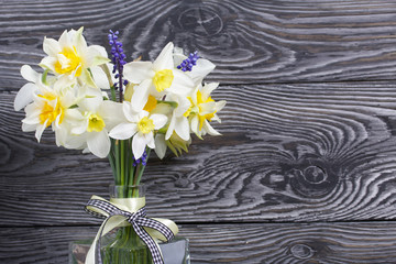 Bouquet of spring flowers in a bottle. Ordinary and terry daffodils. A ribbon bow is tied to the neck of the bottle. Against the background of brushed boards painted black.
