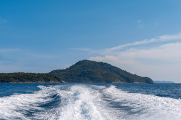 Trace from the motor on the water. Line spray from the ship. Sea, island and sky.