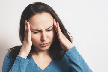 Portrait of a European young woman holding her hands to her temples with a severe headache. On light background.