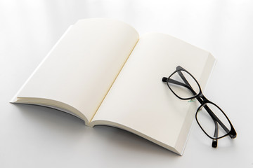 White notebook with eyeglasses on the white background. Blank paper. Blank page. Empty notebook.