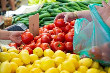 A woman chooses tomatoes in a street market using a plastic bag. Buying fresh organic fruits and vegetables