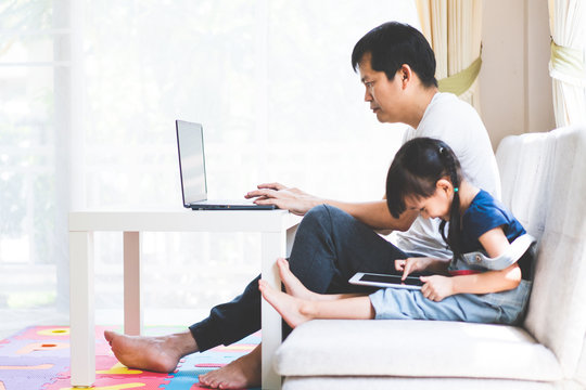 Asian Daddy Is Working From Home In The Living Room And Daughter Sit And Use Tablet Nearly With Him, Concept Of People Lifestyle Changed Impact From Covid 19 Virus Outbreak Around The Word, 