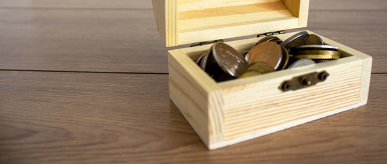 Concept image. Small chest with coins on a beautiful wooden table.