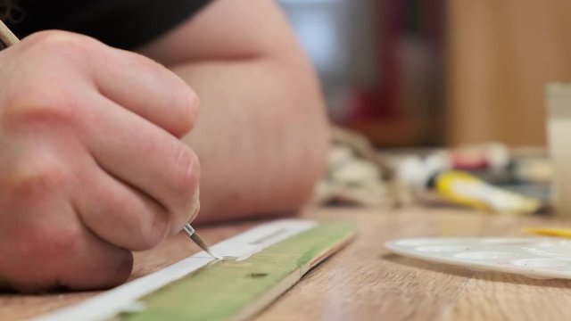 master hand colours wooden old soviet airplane model fuselage with small brush on table at lesson slow motion extreme closeup