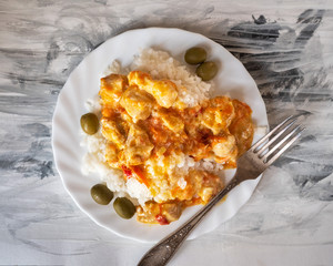 Hearty dinner, a serving of white rice and meat goulash on a round white plate, standing on a black and white napkin, top view