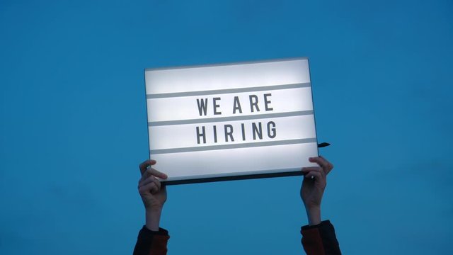 Hands hold up we are hiring sign on isolated sky background. Millennial or generation z hiring boom, surviving economical and financial crisis. Social media industry 