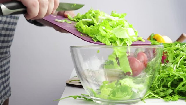 men's hands brush lettuce leaves into a bowl against a background of fresh vegetables and greens, salad preparation, healthy food, vegetarian