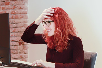 mujer ejecutiva se ríe con la mano en la cabeza y mira el monitor de su ordenador en la oficina 
