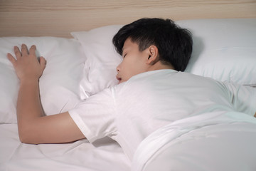 Asian people is sleeping on a white bed in his room. Asian people are tired from work.