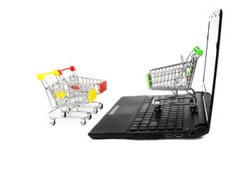 Three empty miniature shopping carts stand close to a black laptop isolated on white. E-commerce concept.