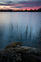 Sunset colors reflected in the surface of a lake with shoreline vegetation.