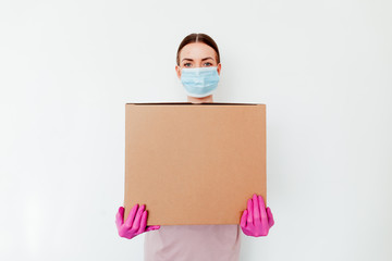 Delivery during coronavirus outbreak. Copy space.  Delivery woman holding cardboard boxes in medical rubber gloves and mask on white background. Online shopping and Express medical delivery .
