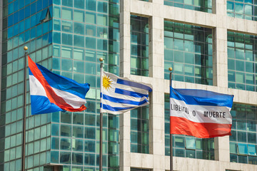 Uruguay - Montevideo - 3 official uruguayan flags (flag of treinta y tres, flag of Uruguay and flag of Artigas) in front of abstract government building on Independence square (Plaza Independencia)