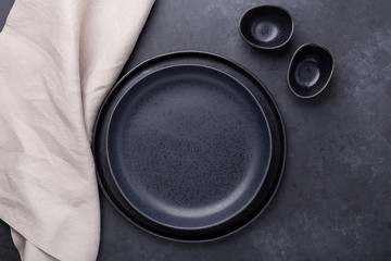 Set of empty ceramic plates and linen napkin on dark stone background Copy space Top view