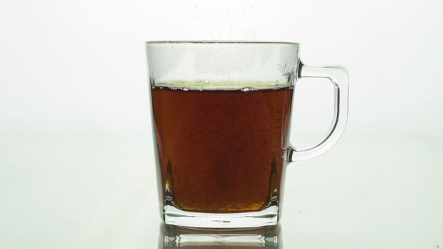 Sugar adding to transparent glass mug with black tea isolated on white background slow motion close up.