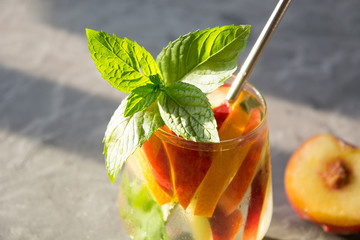 Freshness peach lemonade in glass garnish mint on grey background. Summer shadow.