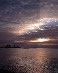 Naklejka premium sunrise through the clouds with lighthouse