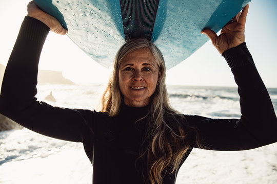 Portrait of smiling senior woman carrying surfboard on beach