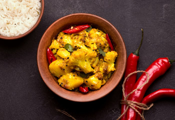 gobi aloo Indian vegetarian dish in a clay bowl on a black background.