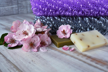 Bath, bathhouse, and spa accessories: handmade washcloths lilac and gray colors, soap and apple tree flowers on a gray background. Bodycare organic cosmetics.