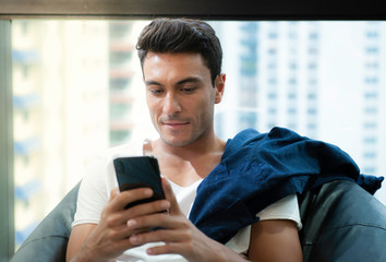 Handsome man sitting on beanbag and using his smartphone againt building background,Cheerful man sitting and using his smartphone at home in the living room.