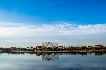 Horizon dividing a blue sky with clouds and a river with reflection of the sky and houses