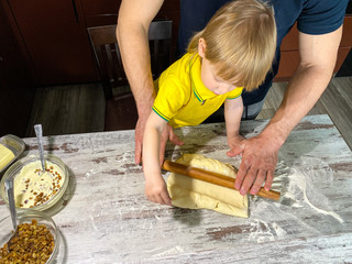 A fair-skinned little child with his father / grandfather prepares sweet rolls filled with cottage cheese and raisins in the kitchen at home. A step-by-step cooking process.Defocus light background.