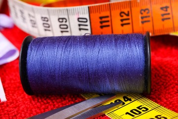Sewing work concept: Macro close up of isolated blue thread spool, scissors and measuring tape