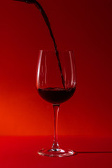 pouring red wine in a glass wine glass on a long leg on a red background