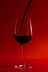 pouring red wine in a glass wine glass on a long leg on a red background