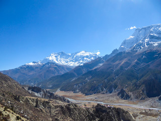 A panoramic view on Manang valley from Praken Gompa, Nepal. High Himalayan ranges around. There is a small torrent in the valley. Snow capped peaks of Annapurna Chain. Harsh landscape.