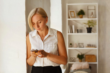 Young businesswoman working using her smartphone sending text message standing near window