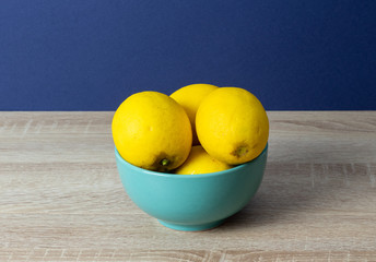 Plate with fresh lemons on the table against the blue wall background