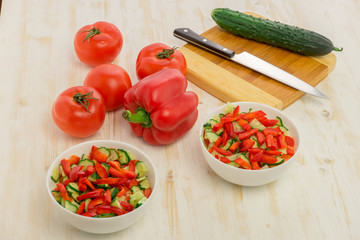 White bowls with fresh salad of green cucumbers, red tomatoes and bell peppers on light wooden surface. Vegetables. Lowcalorie vitamin dietary food. Concept of healthy lifestyle