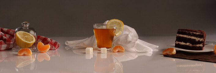 Tea panorama with lemon, sugar and a piece of cake on a white glossy table