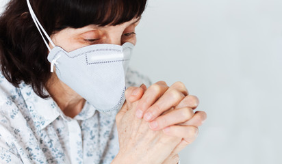 Coronavirus quarantine Covid-19 concept. Face of old sick woman wearing respirator mask for protect praying with folded hands. Wuhan, China epidemic virus symptoms background.