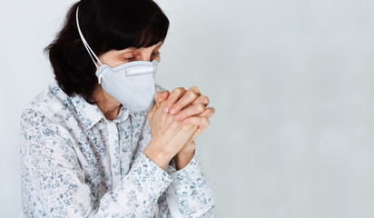 Coronavirus quarantine Covid-19 concept. Old sick woman wearing respirator mask for protect praying with folded hands. Wuhan, China epidemic virus symptoms background.