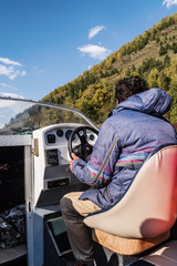 Skipper at the helm of a motor boat, view from the cockpit. Fall. Russia, Altai Republic, Lake Teletskoye