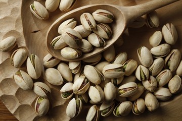 Pistachios in a wooden spoon on wooden textured background.. Selective focus. Wood bowl filled with green pistachio nuts with cracked shell. 