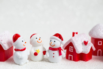 Three smiling toy snowmen, red houses with snow-covered roofs on a white background, a festive Christmas concept