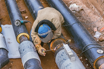 Welder worker welds new metal pipe on the construction site.
