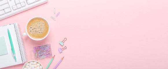 Woman office workplace with cup of coffee and pastel colorful stationery accessories on pink background. Horizontal banner