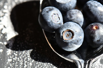 macro photo of blueberries in a silver desert spoon on black background 