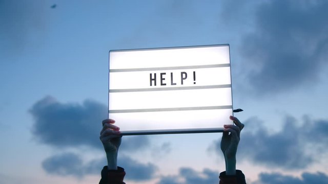 Cry for help electric sign held up in night sky. Motivating and inspiring message for new millennial z generation of boomers. Sign of new times and need for help for small business owners