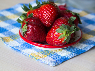 Strawberry background. A plate of fresh strawberries sits on a checkered tablecloth on a wooden table, copy space. Sweet, ripe strawberries. Harvest of organic local strawberries. Healthy food.