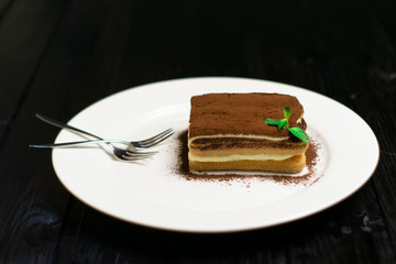Chocolate cake on a white plate and wooden board background.