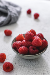 Fresh ripe raspberries in a small plate on light gray table