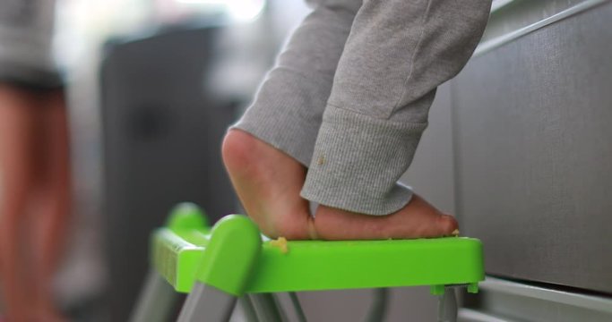 Child on tiptoes at kitchen helping mother. Infant one year old baby feet on tiptoe